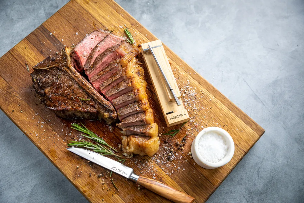 Nuevo termómetro de MEATER encima de una tabla de cortar al Aldo de una carne cocinada